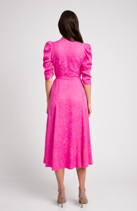 Różowa midi sukienka z bufiastymi rękawami, subtelną kwiatową teksturą, dopasowanym górą i rozkloszowanym dołem. Noszona z cielistymi szpilkami.