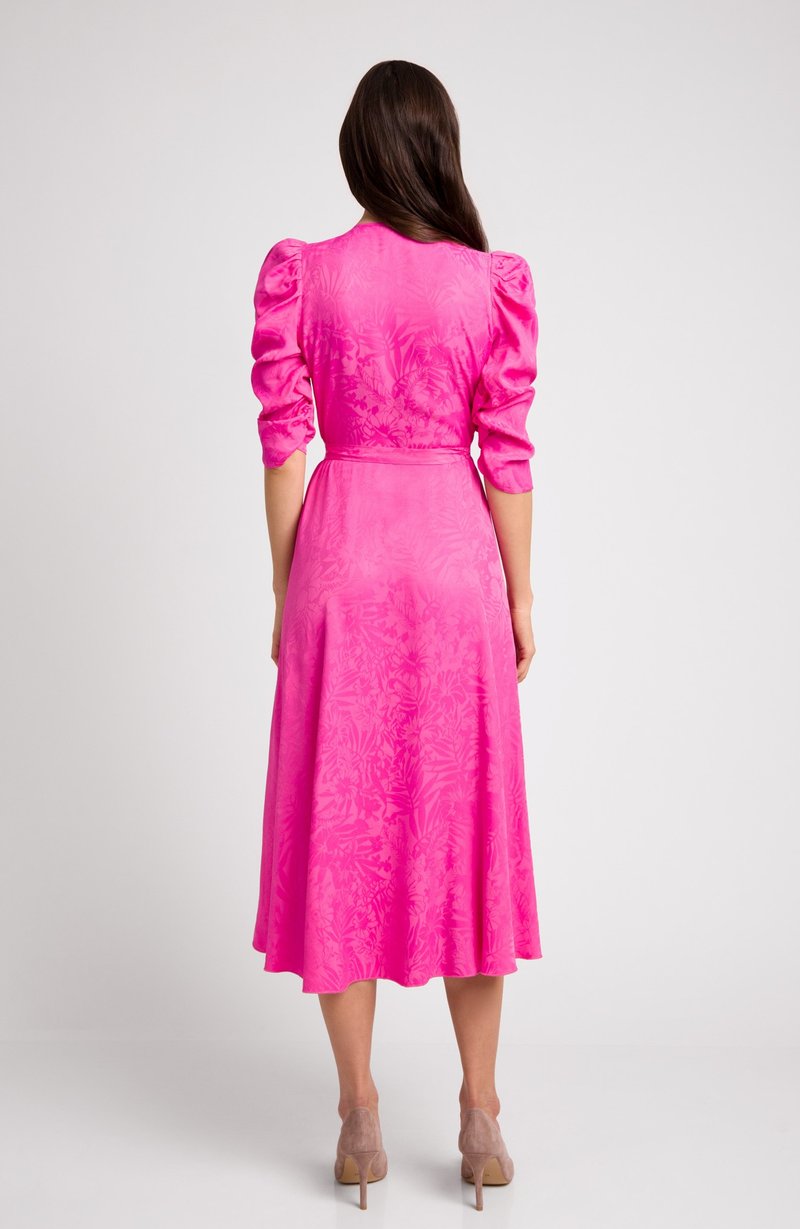 Różowa midi sukienka z bufiastymi rękawami, subtelną kwiatową teksturą, dopasowanym górą i rozkloszowanym dołem. Noszona z cielistymi szpilkami.