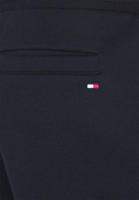 Mörk marinblått tyg med en horisontell ficköppning och en liten rektangulär logotyp i röd, vit och blå nära fickan.