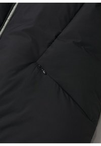 Section en tissu matelassé noir zippée d'une veste matelassée avec une couture diagonale et un petit tire-zip.