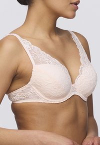 Koronkowy biustonosz w delikatnym brzoskwiniowym kolorze, z głębokim dekoltem, kwiatowym wzorem, przezroczystymi koronkowymi akcentami na ramiączkach oraz gładkimi miseczkami.