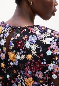 Zwarte jurk met bloemen en pailletten, gekenmerkt door een verscheidenheid aan kleurrijke bloemen en bladeren, met een keyhole sluiting aan de achterkant en een geweven stof.