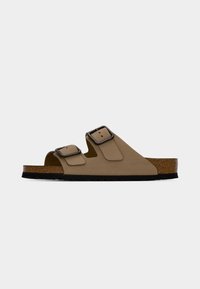 Καφέ δερμάτινο σανδάλι slide με δύο ρυθμιζόμενες μαύρες μεταλλικές αγκράφες και πάτο από φελλό σε μαύρη σόλα, πλαϊνή όψη σε λευκό φόντο.