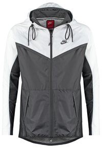 Nike-jacka med lättviktsmaterial, grå och vit färgblockering, huva med dragsnören och två fickor i sidan med dragkedja.