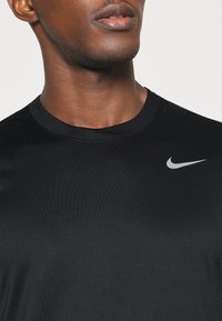 Černé tričko Nike s kulatým výstřihem, krátkými rukávy a malým stříbrným logem na hrudi, vyrobené z hladké, lehké látky.