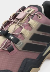 Крупен план на розово и черно обувка за открито с материал GORE-TEX и еластични връзки с лесно издърпване, закрепени с розов стопер.
