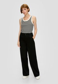 Gestreiftes schwarz-weißes Tanktop kombiniert mit schwarzen weit geschnittenen Hosen und weißen Sneakers, mit einer lässigen Passform und minimalen Details.