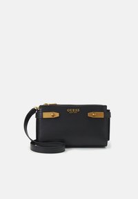 Wristlet nera di Guess con dettagli in metallo dorato, chiusura con zip e cinturino da polso nero abbinato su sfondo bianco.