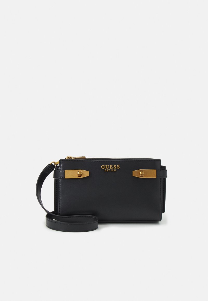 Wristlet nera di Guess con dettagli in metallo dorato, chiusura con zip e cinturino da polso nero abbinato su sfondo bianco.