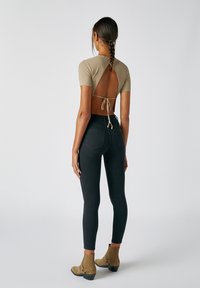Top de manga corta de canalé beige con espalda descubierta y cierre de lazo, combinado con jeans ajustados negros de cintura alta y botines tobilleros color tostado.