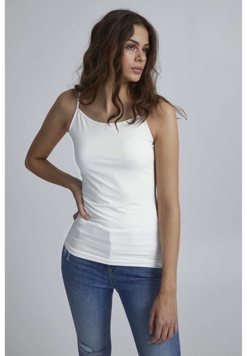Weißes, eng anliegendes Tanktop mit dünnen Trägern, glatter Textur und minimalistischem Design, kombiniert mit ausgebeulten blauen Jeans.