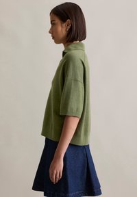 Zielona koszulka polo z krótkim rękawem, uszyta z miękkiego dzianiny, z kołnierzykiem, zestawiona z ciemnoniebieską spódnicą dżinsową o rozkloszowanym kroju.