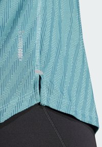 Haut de sport bleu clair avec motif texturé et fentes sur les côtés, arborant la marque "CLIMACOOL+", associé à un bas noir.