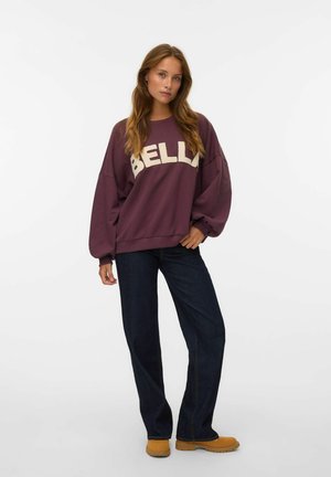 Bordo sweatshirt s tekstom "BELLA" v kremni barvi, ohlapen dizajn, kombiniran s temno modrimi širokimi hlačami in svetlo rjavimi klobuki. Enobarvne barve, sproščen slog.