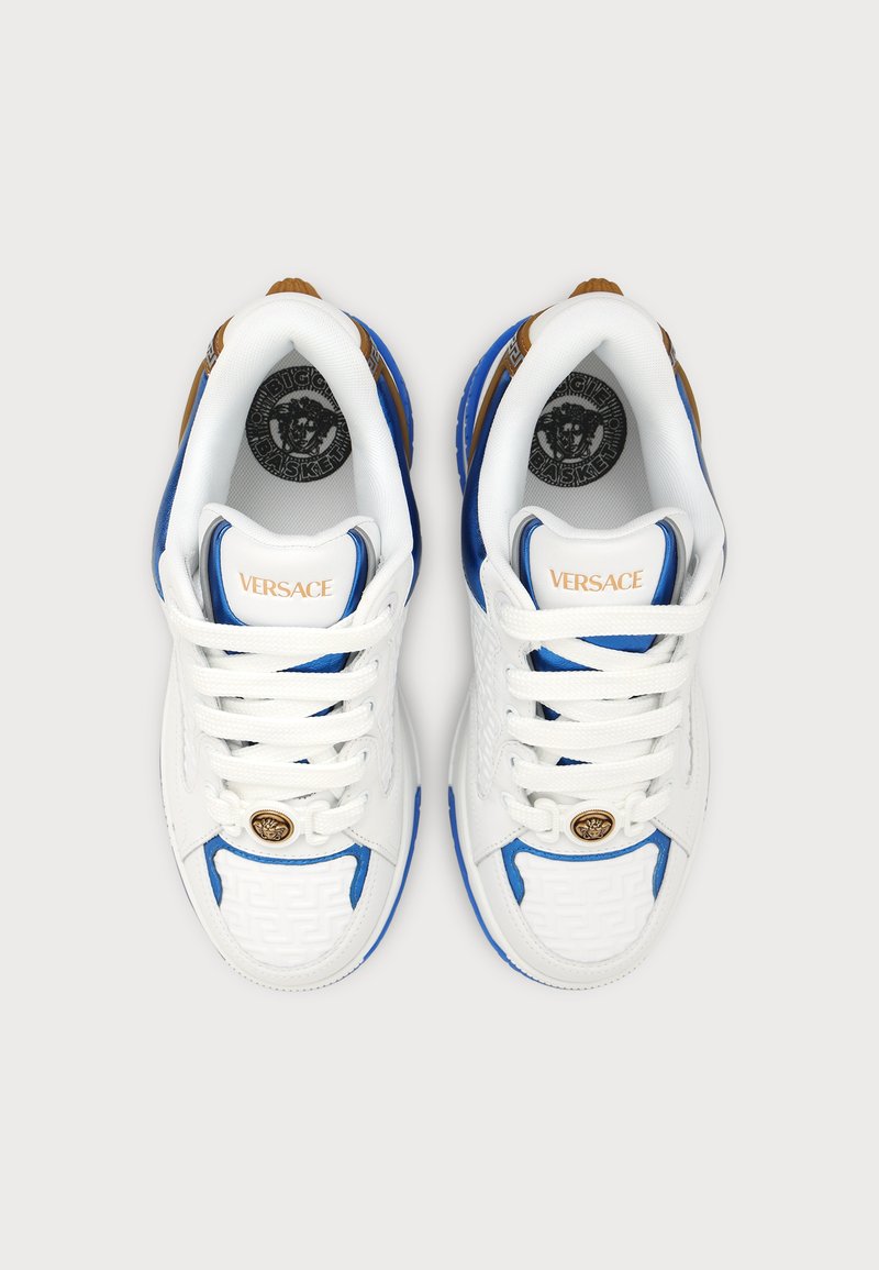 Ein Paar weiße Versace-Sneaker mit blauen und goldenen Akzenten, Medusa-Logo auf Zunge und Sohle, von oben vor neutralem Hintergrund betrachtet.