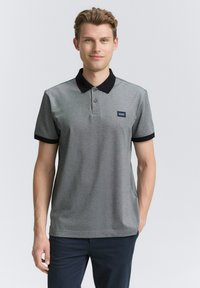 Grå polo t-shirt med sort krave og ærmeakcenter; har tre knaplukninger og lille logo-patch på venstre bryst. Casual pasform.