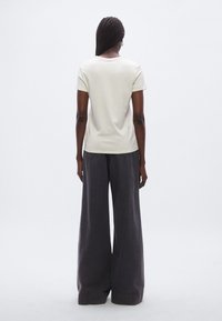 Jasnobeżowy t-shirt z krótkim rękawem w połączeniu z szerokimi spodniami o ciemnoszarym kolorze, prezentujący luźny krój i gładką fakturę od tyłu.