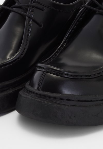 Zapatos de cuero negro con un acabado brillante, puntera redondeada, costuras distintivas y una suela de goma gruesa y texturizada.