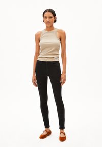 Débardeur beige à côtes, jeans skinny noirs et ballerines marron. La tenue présente un design minimaliste avec des lignes épurées et des couleurs contrastantes.