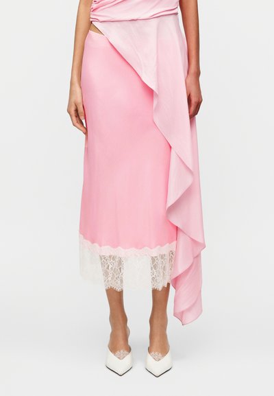 Jupe en satin rose avec un design à volants en cascade et un bord en dentelle blanche à l'ourlet, associée à des chaussures blanches à bout pointu.