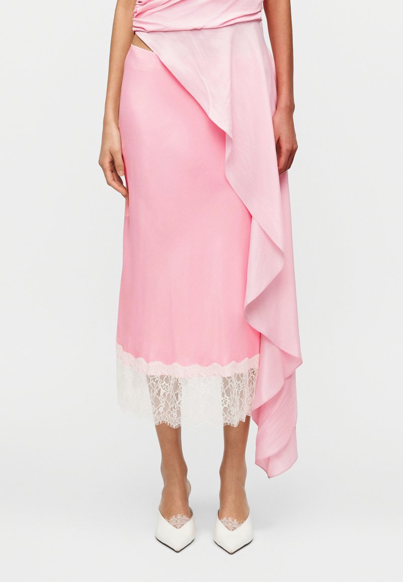 Ροζ σατέν φούστα με καταρράκτη από βολάν και λευκή δαντέλα στο τελείωμα, συνδυασμένη με λευκά παπούτσια με μυτερή μύτη.