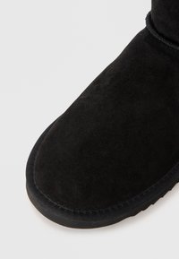 Black suede ankle boot with a rounded toe, smooth texture, and a rubber sole. Stitching along the edge adds detail to the design.