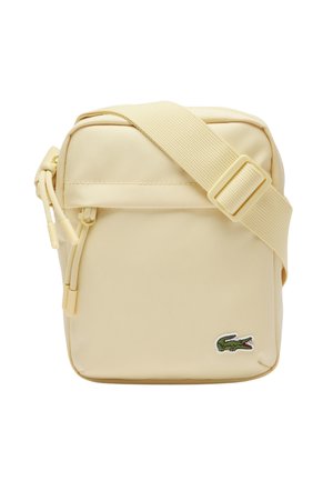 Small beige crossbody bag with adjustable strap, zipper closure, and green crocodile logo on front corner.