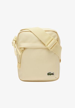 Kleine beige crossbodytas met verstelbare riem, ritssluiting en groen krokodillenlogo op de voorhoek.