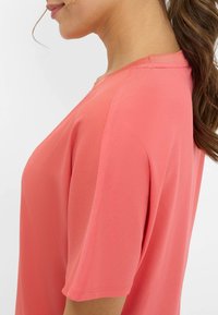Coral short-sleeve top with a smooth texture and loose fit, featuring a rounded neckline and shoulder seam details.
