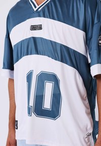 Uomo che indossa una maglia sportiva blu e bianca con il numero 10, il logo PXP Sport e una firma in basso a destra.