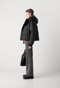 Doudoune noire avec capuche, présentant un design matelassé. Assortie à un jean ample gris et des chaussures à plateforme noires, tenant un sac fourre-tout noir.