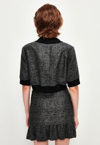 Mustekka ja harmaata tweed kangasta oleva lyhythihainen crop-top, jossa on ribbireunus, yhdistettynä samanlaiseen rypytettyyn hameeseen. Rakennekangasta.
