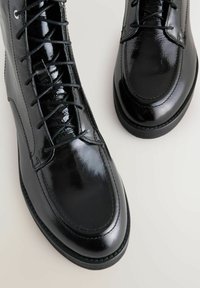 Stivali in pelle nera con finitura lucida, punta rotonda e design con lacci. Cuciture di dettaglio lungo le cuciture aggiungono consistenza.