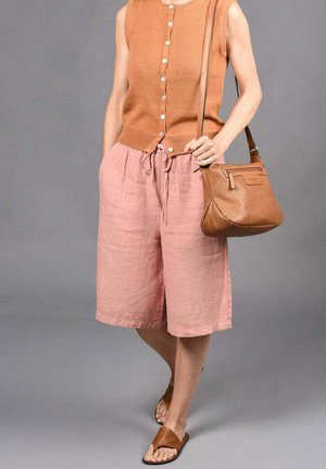 Tan gebreide mouwloze top met knopen, gecombineerd met losse roze linnen shorts en een bruine geperforeerde handtas. Bruin sandalen maken de outfit compleet.