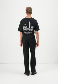 Black cotton T-shirt with a white graphic of Tower Bridge and a clock tower on the back, paired with black trousers and shoes.