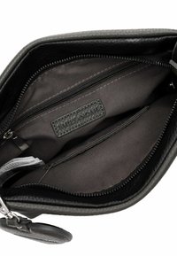 Black leather handbag interior featuring zippered and open compartments, textured lining, and a brand label patch. Smooth, durable material.