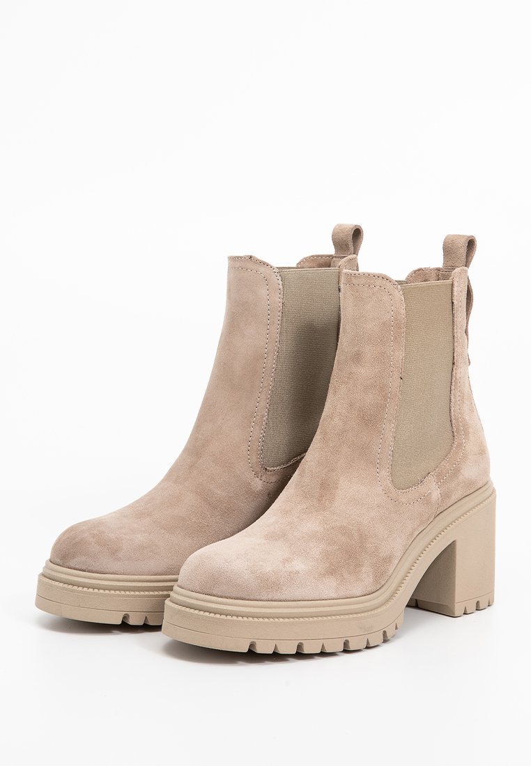 Beige Wildleder-Ankle Boots mit dicken Absätzen, elastischen Seitenpaneelen und Zugschlaufen auf der Rückseite, auf einem weißen Hintergrund.