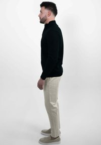 Zwarte gebreide trui met een hoge hals, gecombineerd met lichte beige broek en beige instappers, heeft een gestroomlijnd silhouet.