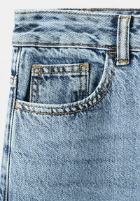Jean en denim bleu clair avec poche avant, coutures orange et passants de ceinture visibles sur fond blanc.