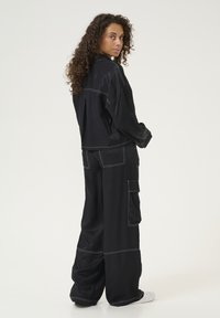 Giacca nera oversize e pantaloni cargo con dettagli in bianco, realizzati in tessuto morbido, caratterizzati da una vestibilità rilassata e tasche laterali.