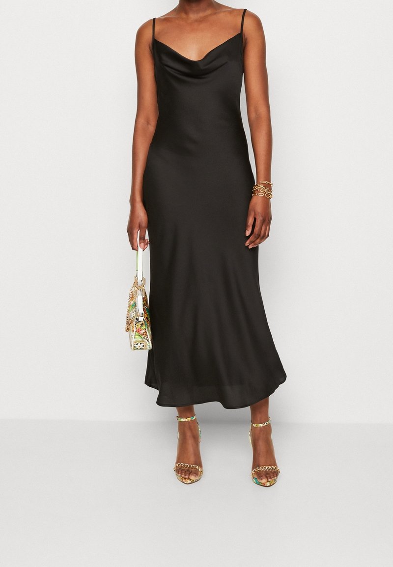 Zwarte satijnen midi-jurk met een draperende halslijn en dunne bandjes. Model gestyled met een kleurrijke tas en metalen sandalen met hak.