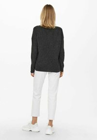 Szary sweter z dzianiny o luźnym kroju, okrągłym dekolcie, długich rękawach i ściągaczami, w połączeniu z białymi spódnicami o kroju cropped i białymi trampkami.