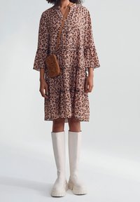 Šaty s leopardím vzorem, s nabíranými rukávy, zdobené v několika vrstvách a s výstřihem do V; doplněné béžovými platformovými botami po kolena a malou hnědou crossbody kabelkou.