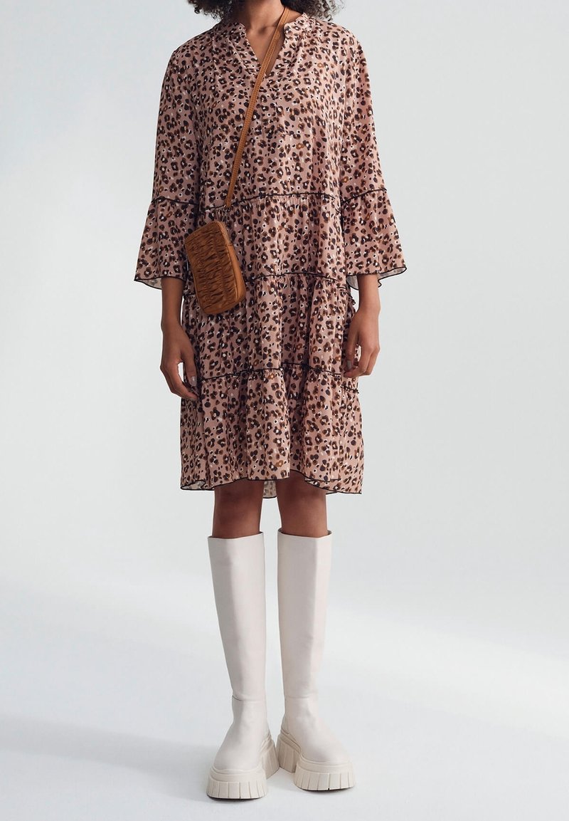 Šaty s leopardím vzorem, s nabíranými rukávy, zdobené v několika vrstvách a s výstřihem do V; doplněné béžovými platformovými botami po kolena a malou hnědou crossbody kabelkou.