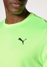 Green athletic shirt made of smooth fabric, featuring a black Puma logo on the chest. Crew neck design with short sleeves.