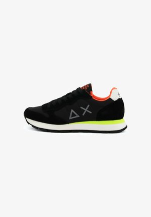 Czarny sneaker z neonowo zielonym paskiem na podeszwie środkowej, pomarańczową wyściółką wewnętrzną, białą łatą na pięcie, szarym geometrycznym logo i czarnymi sznurowadłami, widok z boku.