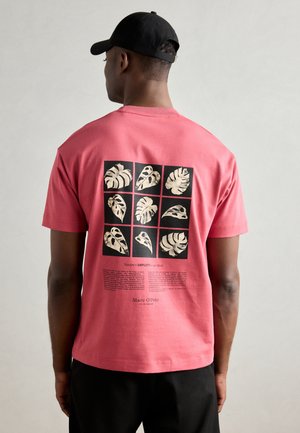 Pink bomulds t-shirt med et grafik af ni botaniske illustrationer på en sort baggrund, med hvid tekst underneden.