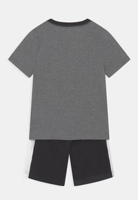 T-shirt grigia in cotone a maniche corte e collo rotondo, abbinata a pantaloni corti neri con accenti bianchi sui lati e vita elastica.