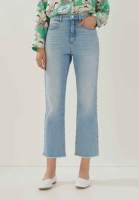 Jeans azzurri a vita alta con un taglio a gamba larga cropped, caratterizzati da un orlo sfilacciato e una leggera scoloritura. Abbinati a scarpe bianche slip-on.