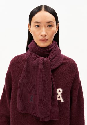 Burgunderfarbener Strickschal mit strukturiertem Rippmuster, das ein kleines Logopatch trägt. Komplementär zu einem weichen, burgunderfarbenen Pullover.